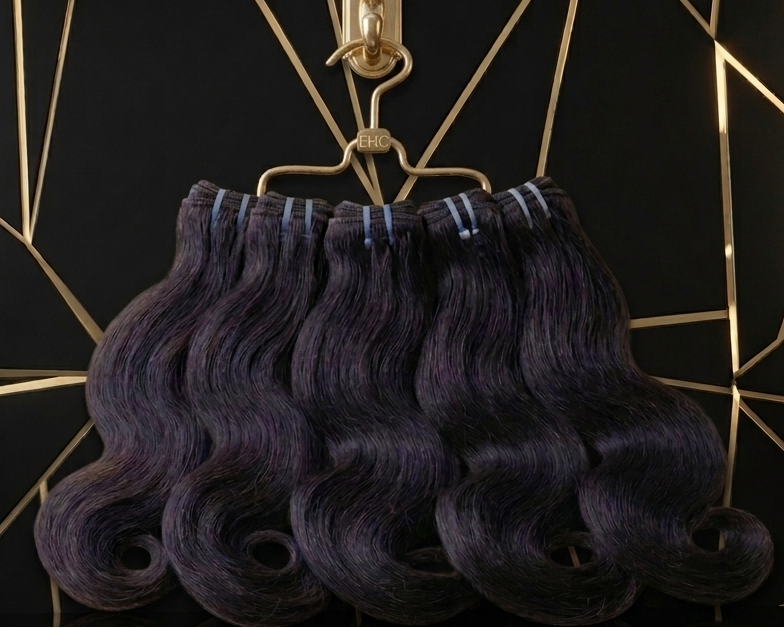 Three bundles of body wave hair extensions in a deep purple shade, hanging from a gold metal clip against a black background with a gold geometric line pattern.